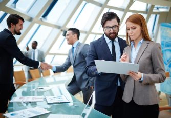 Business life Two business people discussing data or planning work on background of their colleagues handshaking